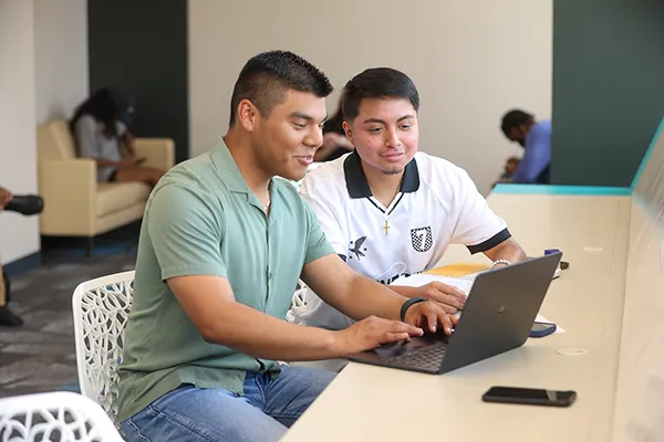 two students sitting in front of a laptop