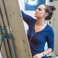 A female student painting while wearing earbud headphones 