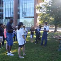 An outdoor art lecture with an easel visible, students looking on 