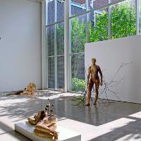 An art exhibit of three lifelike figures, one crawling, one on their side, one standing; all have wounds and thorns or branches coming out of them 