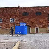 A man on a bike pulling a large blue box 