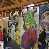 Large painted artworks hanging from the ceiling, students looking on  