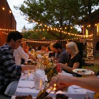 several tables of people eating outside, string lights running across the top 