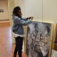 A smiling student preparing to hang her paintings 