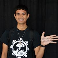 A smiling student with his palm facing the camera. His palm has "Quality In Education" written on it. 