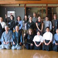 Students holding long wooden objects and guests in kimonos, some kneeling 
