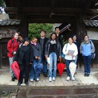 A group of students in traveling clothes, umbrellas, and backpacks, smiling 