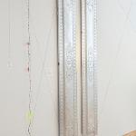 Tall vertical hanging sculpture with translucent beaded strands in gallery