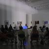 Audience seated in dimly lit gallery watching projected performance