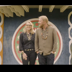 Two people standing together in front of a circular decorative backdrop with a retro aesthetic.