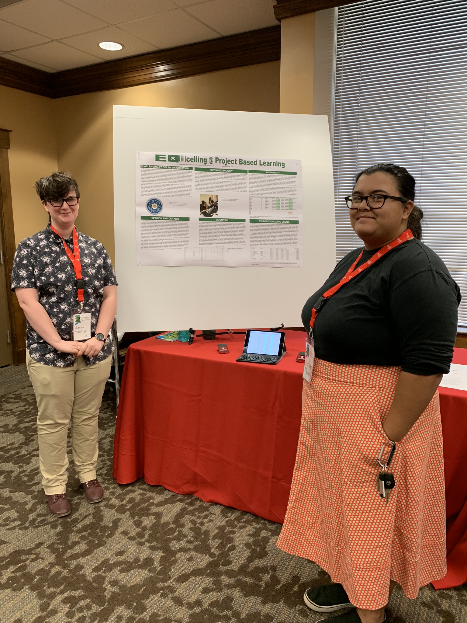 two students standing in front of a poster on a table