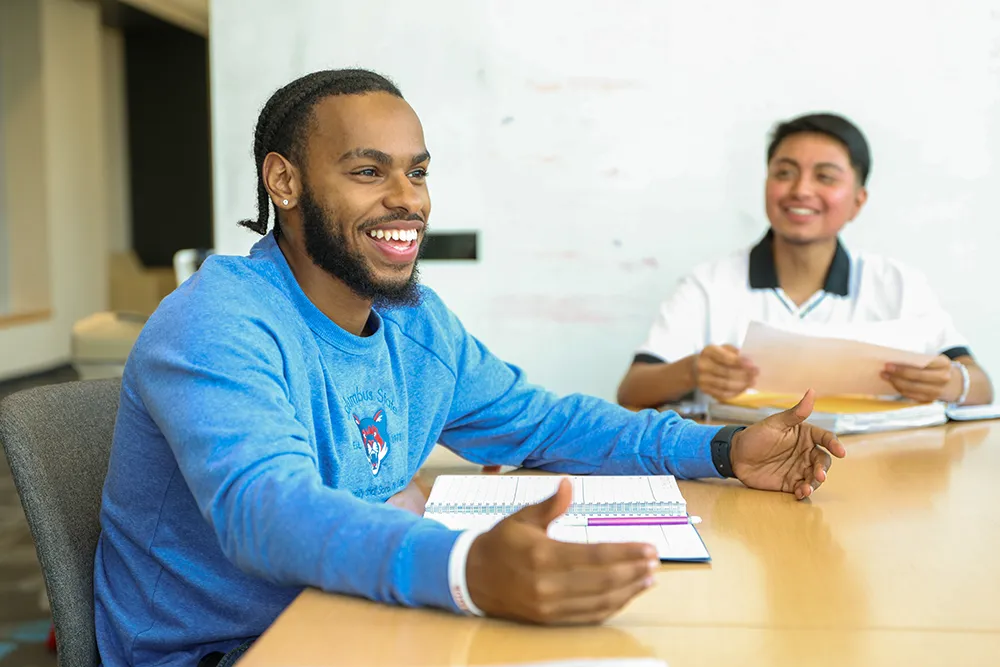 Two graduate students smiling and collaborating at a table