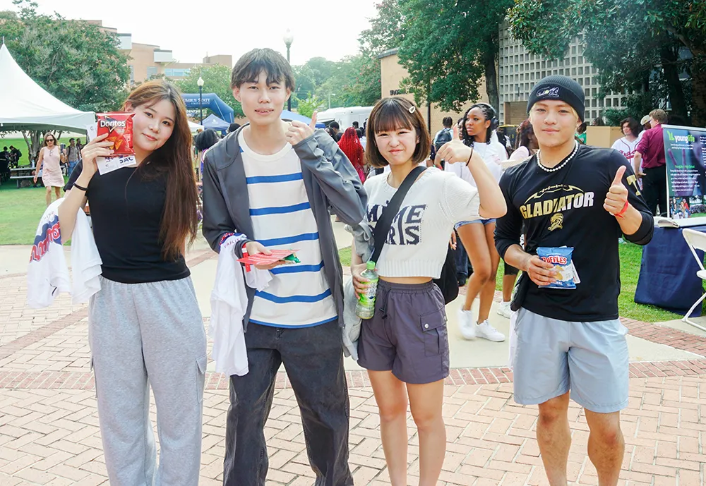 Four students posing together at an outdoor campus event