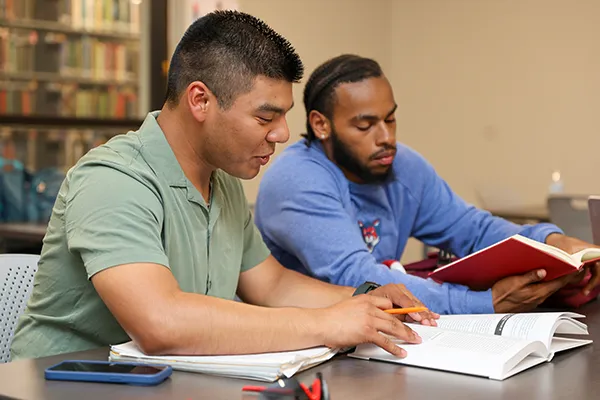 Two students reading textbooks at a library table