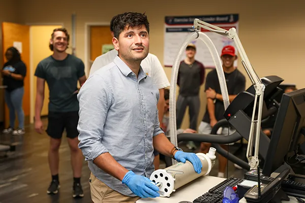 Student in gloves handling lab equipment while classmates observe