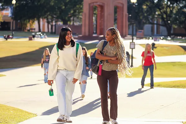 Two students walking and talking on a sunny college campus