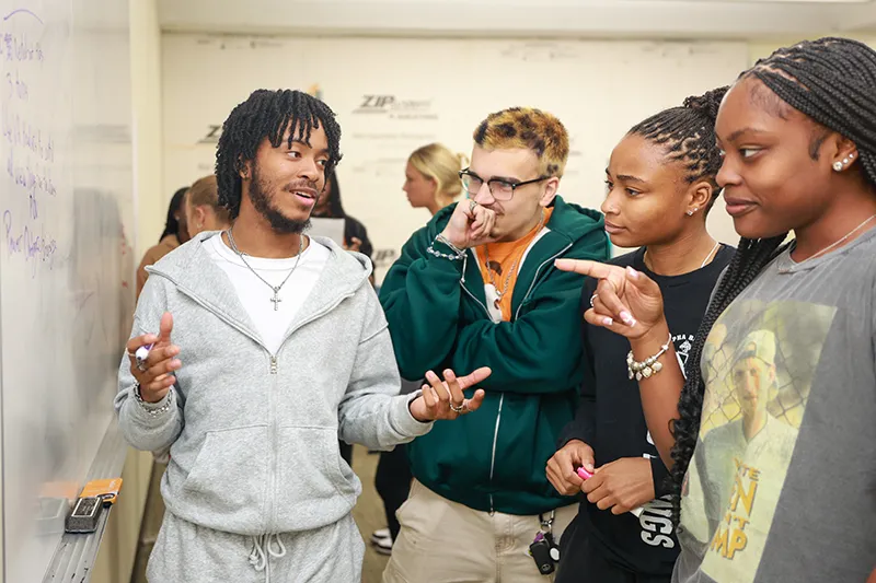 Four students collaborating at a whiteboard during a group activity