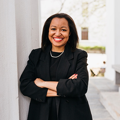 a woman wearing a black suit leaning against a wall with her arms crossed