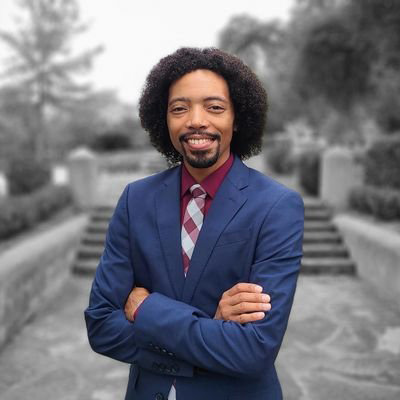 a man wearing a blue blazer and red shirt with his arms crossed
