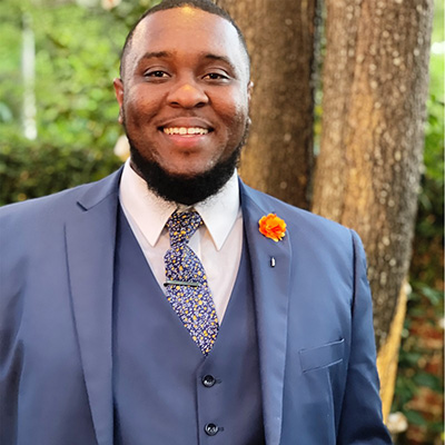 a man wearing a blue suit standing in front of a tree