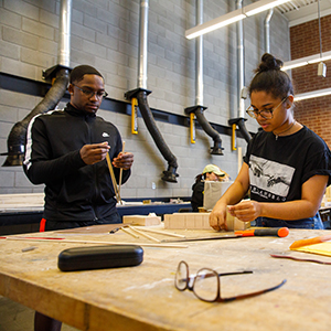 a male and female student working on a wooden art project