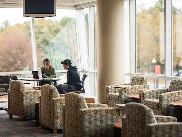 A male and female student sitting in a lobby with laptops