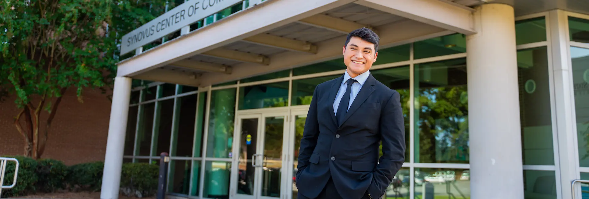 a student in business attire standing in front of the Synovus Center for Commerce and Technology building