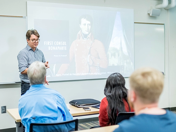 Students listening to a lecture from a professor in a brightly lit classroom