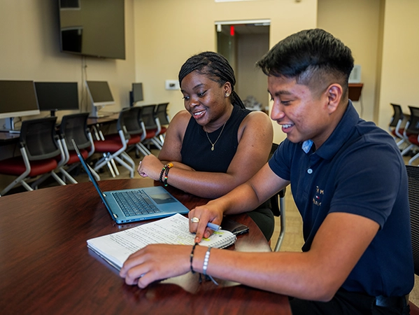 Two students researching together with a laptop and a notebook.