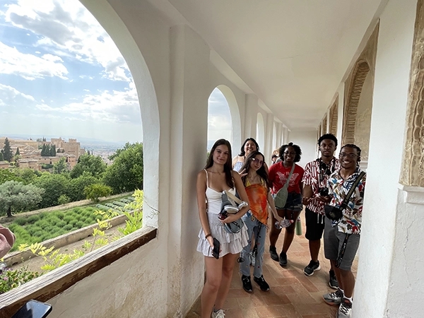 Students posing for a photo in an outdoor hallway looking over a beautiful view of Alcazar Seville.