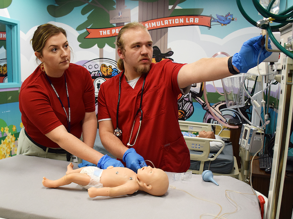 Two nursing students practicing caring for small child doll