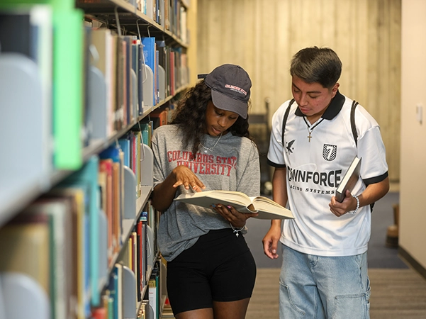 Two students reading a book and researching together in the library.