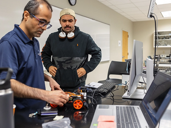 A student watching another student work with parts of a robot.