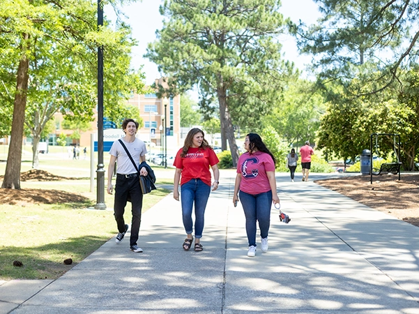 Three students walking on main campus together, smiling and talking.