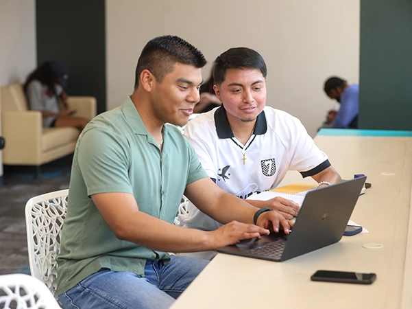 Two students studying together on a laptop at a desk.
