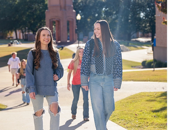 Two students walking on main campus, smiling and talking with eachother.