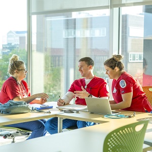 two female and one male students sitting at a table talking to each other