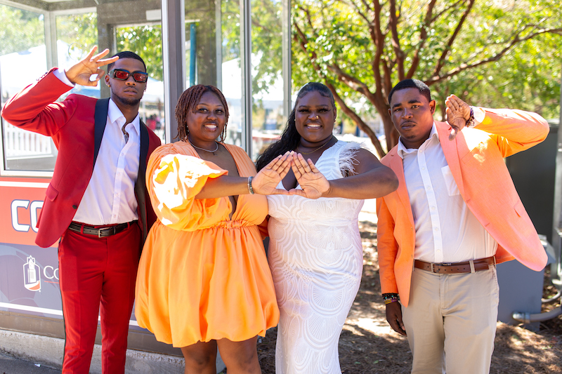 Two sorority and two fraternity members smiling, all dressed in bright formal dresses and suits
