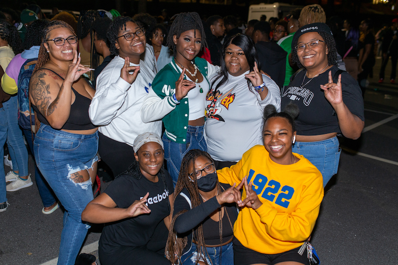 Fraternity and sorority members smiling outside, all making the same hand symbols