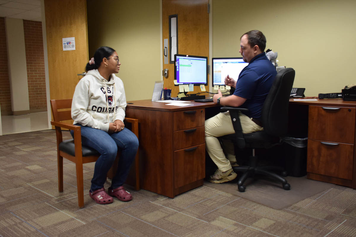 A student in jeans and a CSU hoodie talking with an employee, both seated