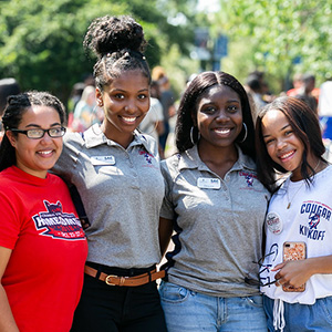 Four students smiling together at an outdoor campus event