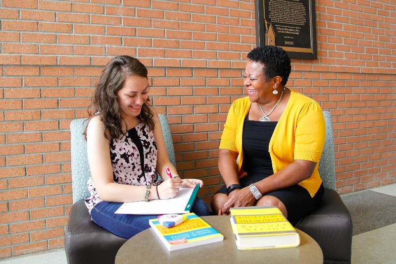 a student taking notes with her mentor sitting next to her, both smiling