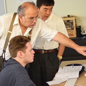 two professors standing and pointing at a screen while a male student watches