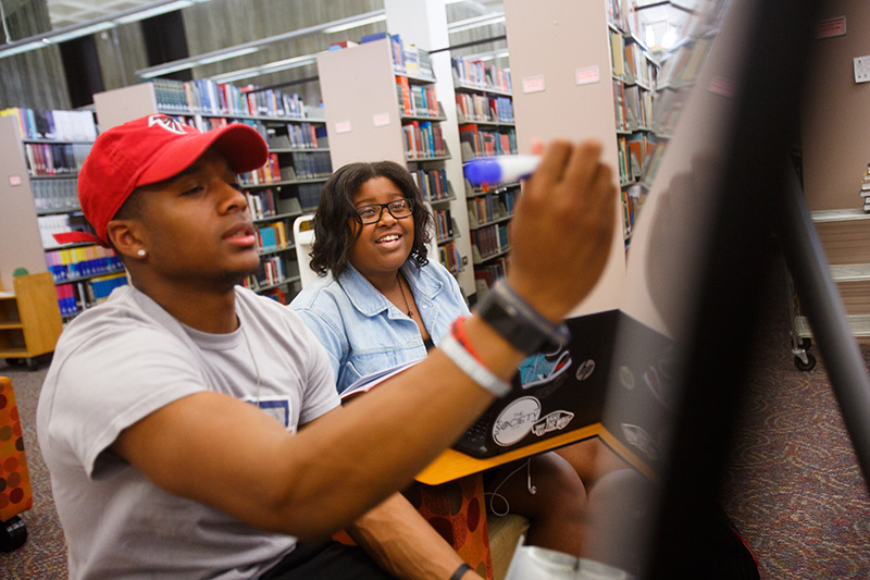 two students looking at and writing on a whiteboard